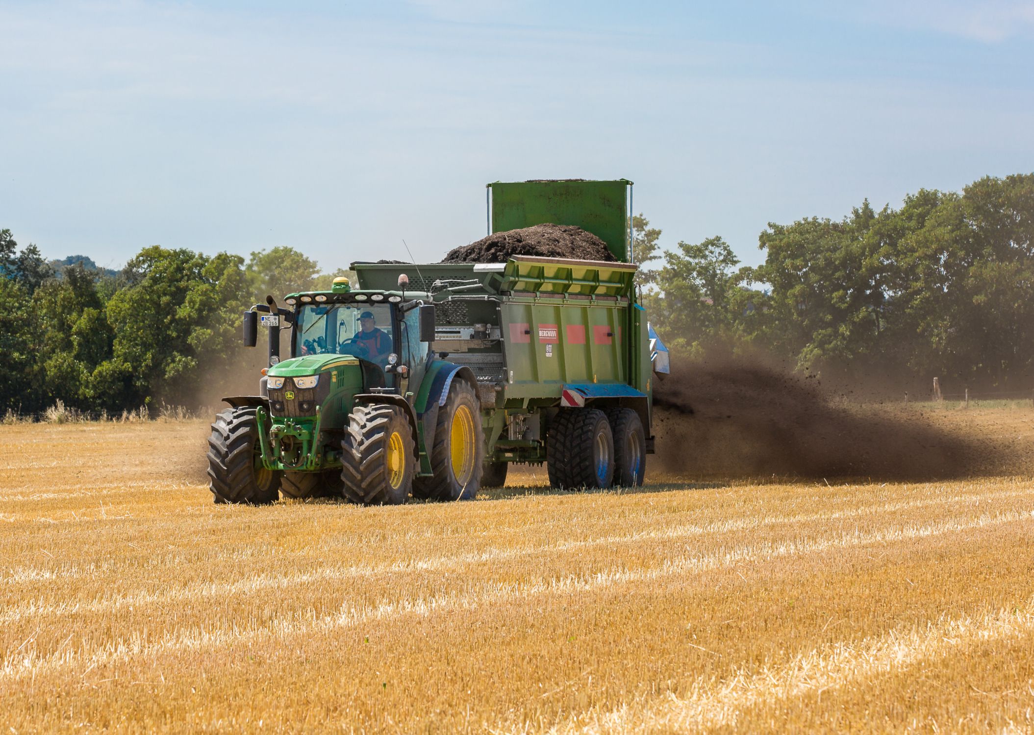 Kompost-Traktor auf Feld grüner Traktor mit Kompost-Anhänger auf gelbem Feld